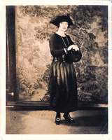 Frederick wearing a dark dress and hat and carrying a purse