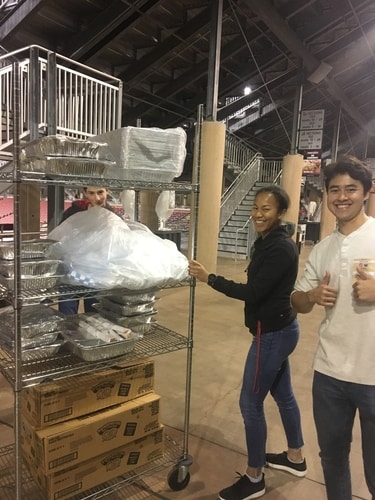 Student volunteers in Stanford Stadium pushing a metal cart of food tins