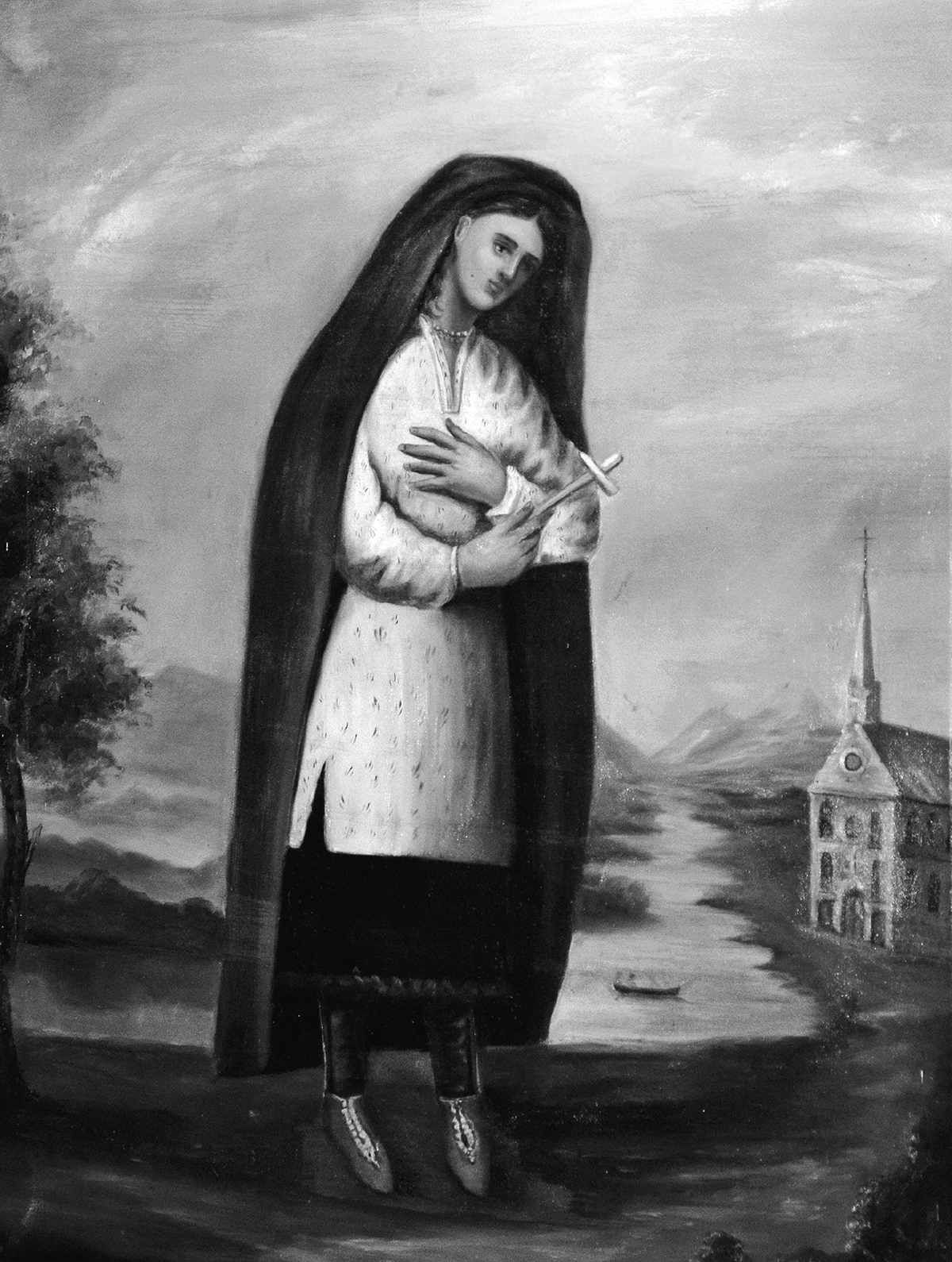 Religious painting of a Native American woman, identified as Kateri Tekakwitha, standing beside a river with mountains in the background. She wears a white tunic adorned with small decorative patterns, a dark cloak over her head and shoulders, dark leggings, and moccasins. Her head is tilted gently to the side in a contemplative pose, and she holds a wooden cross close to her chest with both hands. The setting suggests a serene, spiritual landscape with a canoe or boat on the river below.