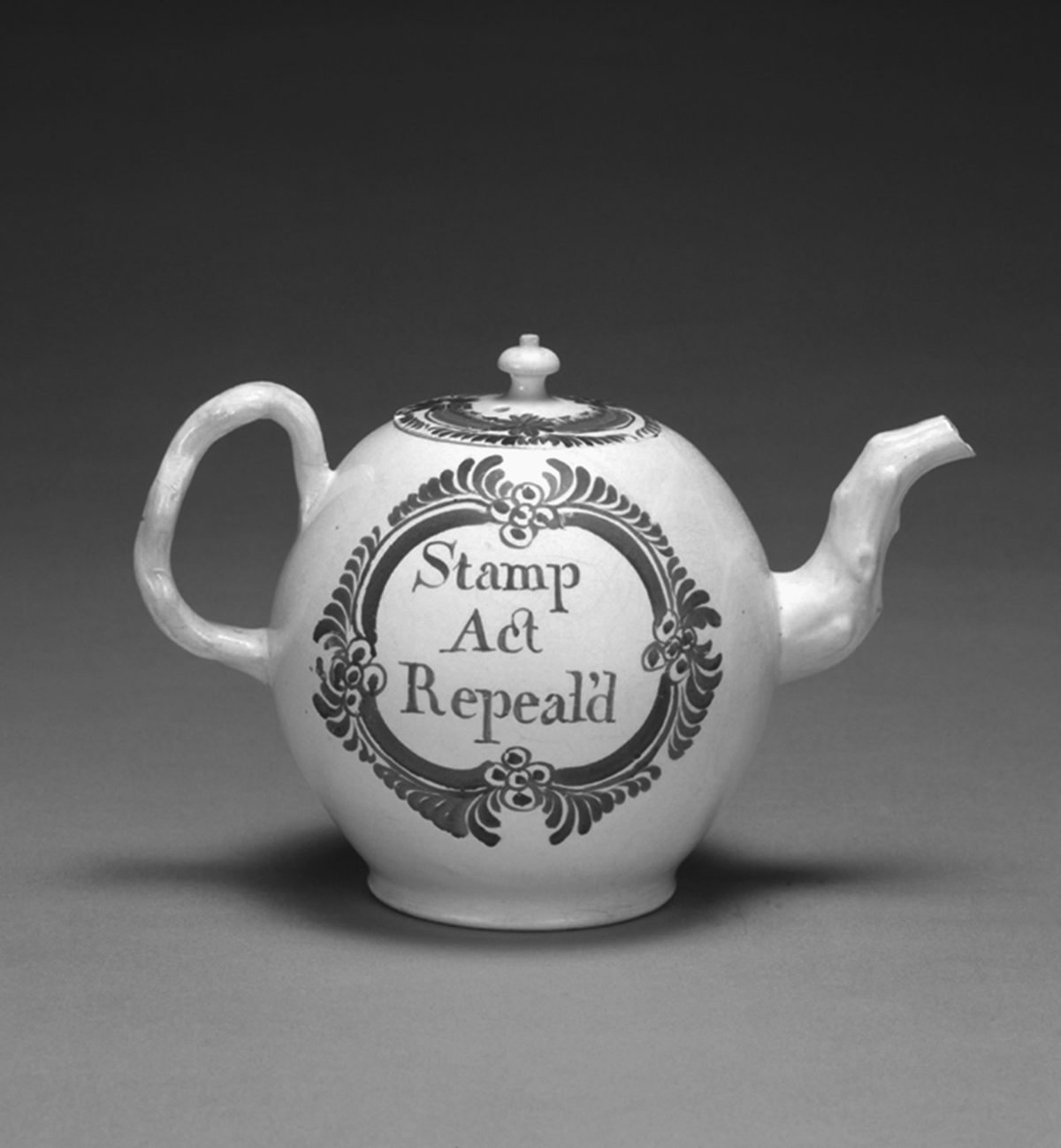 An eighteenth-century British colonial teapot. The teapot is white with a red pattern and red lettering that reads, “Stamp Act Repeal’d.â€