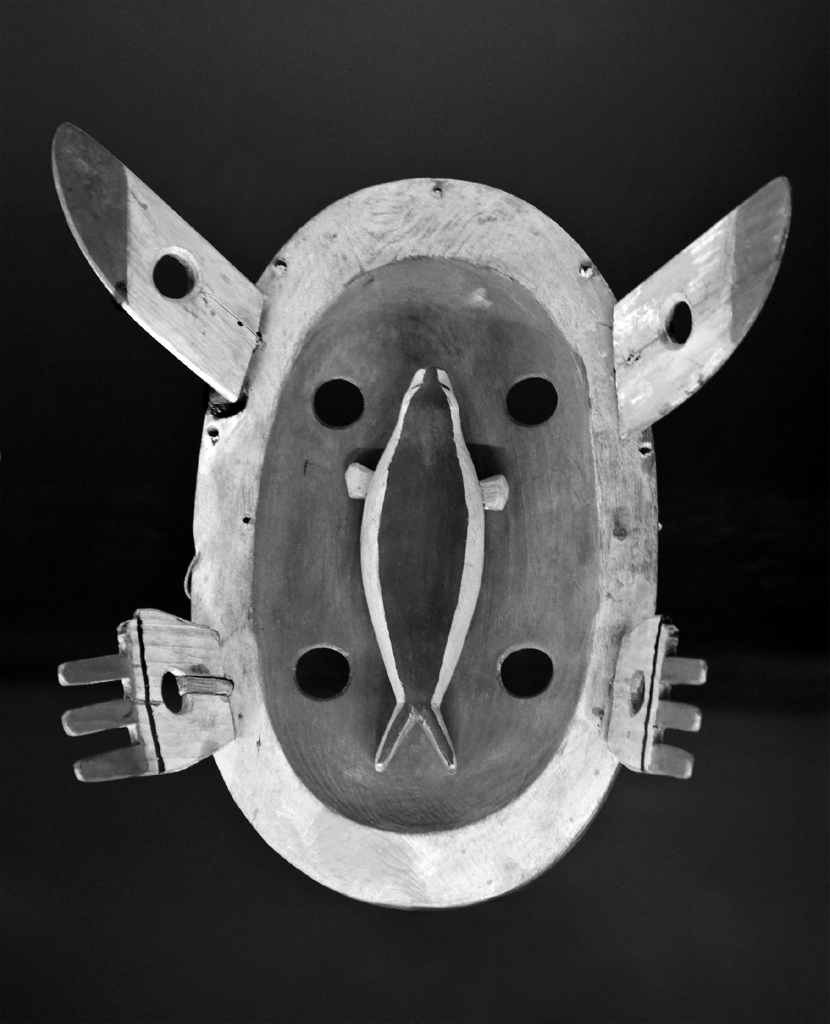 Yupâ€™ik masks are used in ritualistic dances by shamans to connect the natural and spiritual worlds. This mask is in a yellow wood with the figure of a seal, a traditional food for the Indigenous people of Alaska and what appears to be hands and ears that protrude outward.