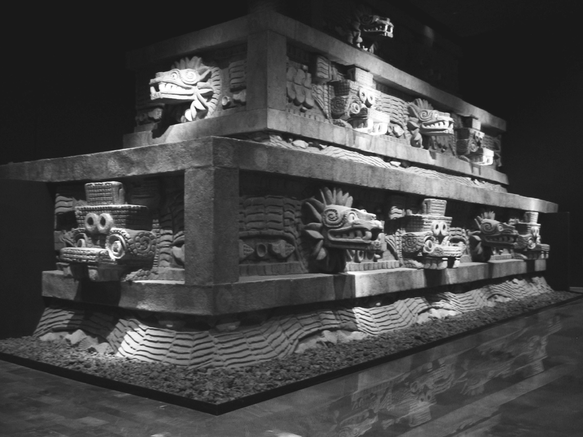 Restored TeotihuacÃ¡n faÃ§ade from the Temple of the Feathered Serpent. The facade is decorated with feathered serpent heads on each side with circles and squares intermittently. The structure is made of jade and painted red and gold.