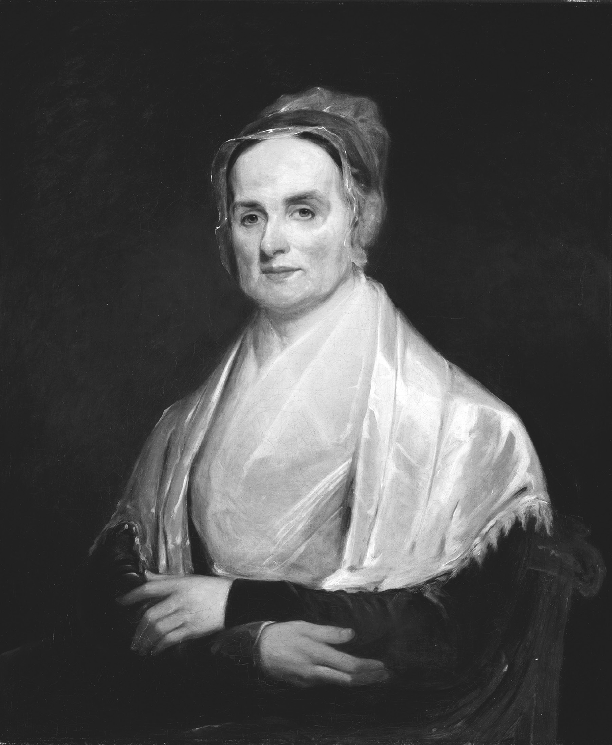 This 1842 oil painting is a portrait of Lucretia Mott by Joseph Kyle. An older woman sits turned slightly to her right, wearing a dark dress almost totally covered by a bright white, shiny shawl and a filmy white neck cloth. Her head is covered by a lacy cap.