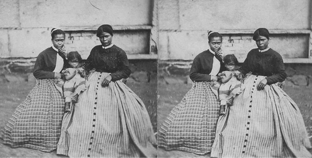 This is a black-and-white photo of Selina Gray and her two daughters. Selina Gray was the enslaved housekeeper of Robert E. Lee. An older woman with dark hair parted in the middle sits with a younger woman and a very small child between them. The two women both wear dresses with voluminous patterned skirts and dark tops. All three figures are facing the viewer.