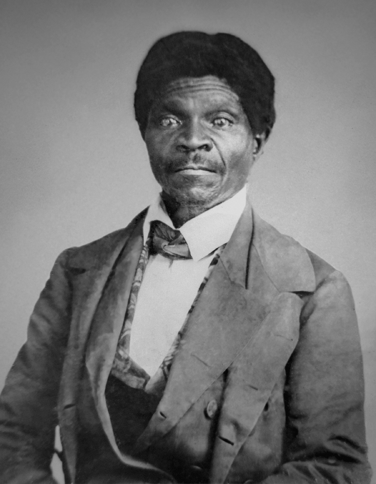 Photograph of Dred Scott, 1857. A Black man with a slight mustache wears a coat over a white shirt and patterned vest with a dark neck cloth. He is turned slightly to his right but faces the viewer.