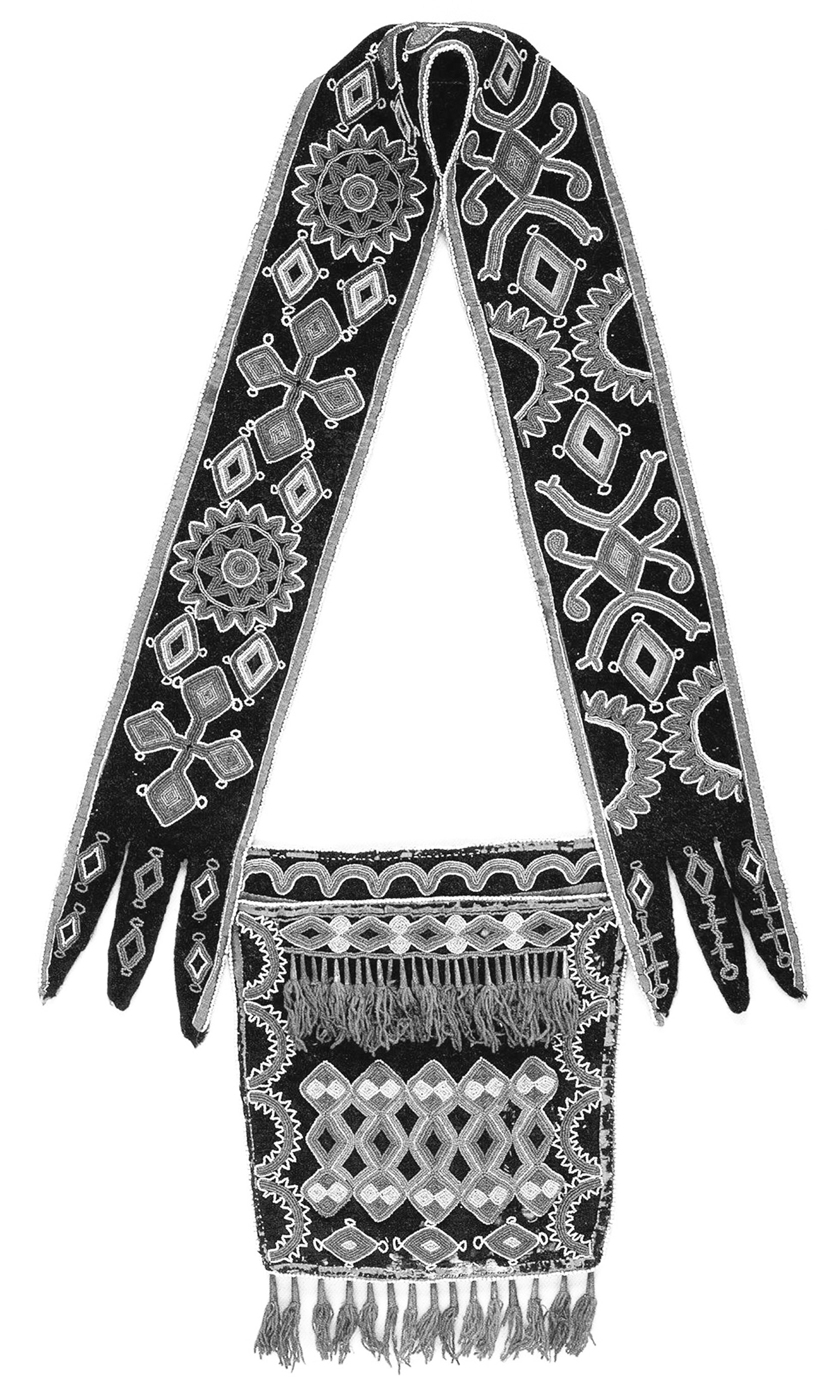 Intricate, multicolored Delaware bandolier bag dating to 1870 is constructed of a black material with a shoulder strap and small bag to be worn to the side. The bag is bordered with a brown fabric and has fringes hanging from the top and bottom of the bag itself.