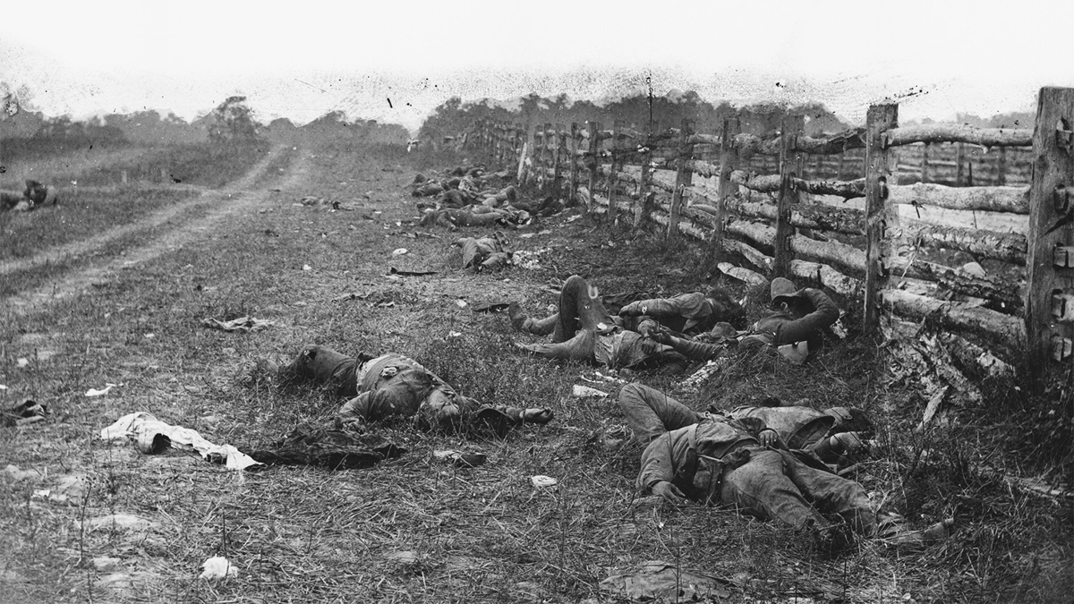 An 1862 photograph by Alexander Gardner of dead Confederate soldiers after the Battle of Antietam. Cart tracks lead away into the distance on the left, and a wooden fence extends along the right, with many bodies and debris lying between.
