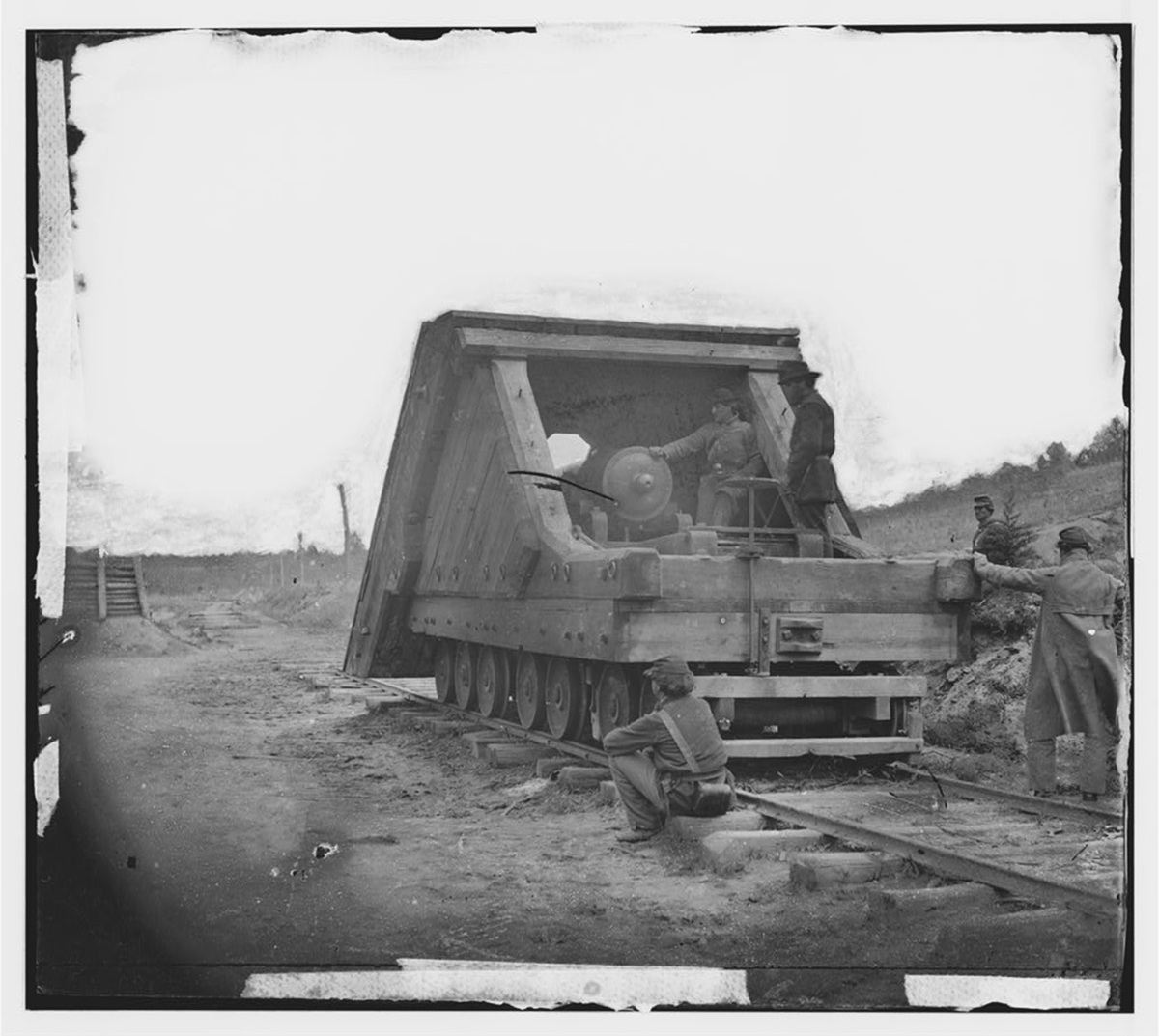 This circa 1864â€“1865 photograph shows Robert E. Leeâ€™s railroad gun and crew used in the main Eastern Theater of war at the siege of Petersburg, Virginia. A large piece of machinery with many wheels runs on a railroad track extending from the right foreground into the middle distance. Two men stand on the machine with several others sit or stand next to it.