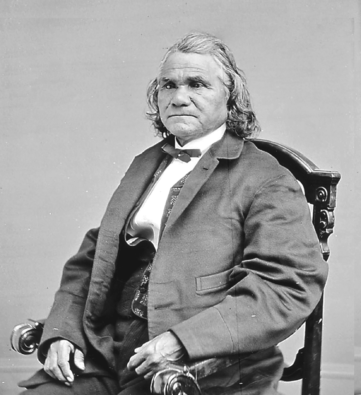 A photograph of Isaac Stand Watie sitting in a chair and looking slightly to his left. He wears pants, dress shirt, vest, and coat with a bowtie. Isaac Stand Watie Degatag, Principal Cherokee Chief, was the last Confederate general to surrender in the Civil War.