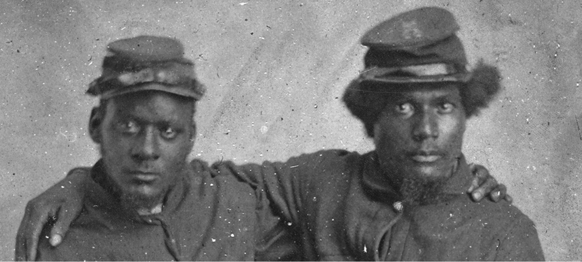 In this photograph titled Two Brothers in Arms, two unidentified Black men pose in military uniforms and caps with their arms around one another, circa 1860â€“1870.