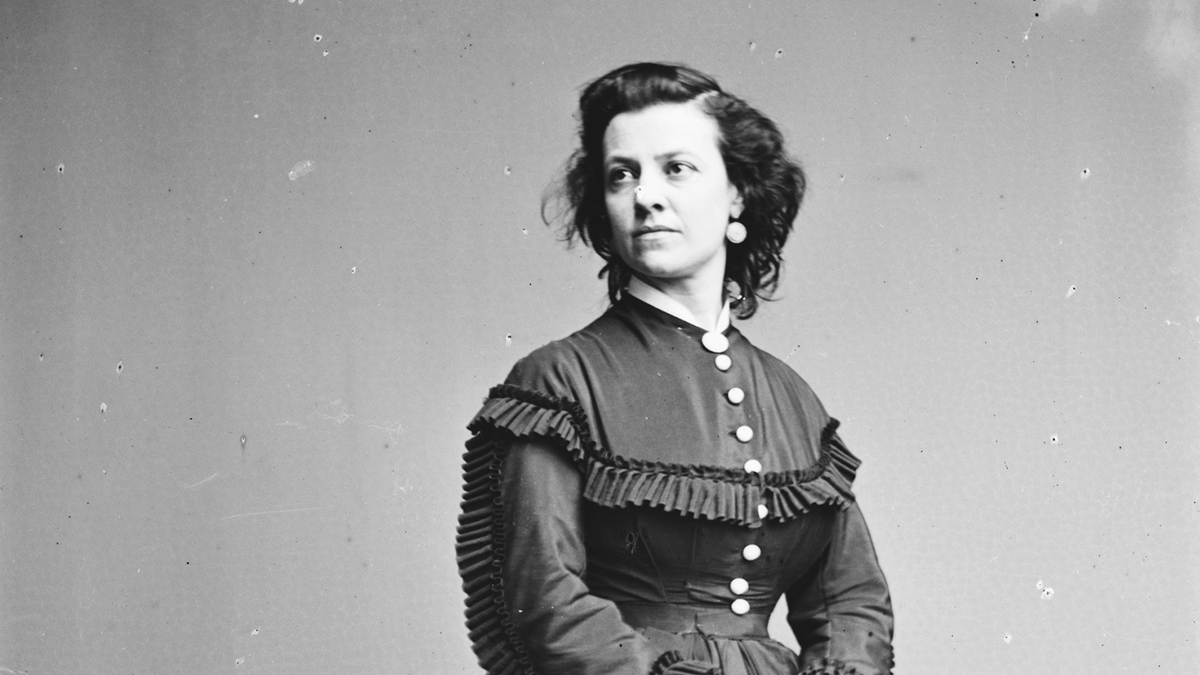 A circa 1855â€“1865 photograph of Pauline Cushman wearing a dark dress with large white buttons and small black fringe along the bust and arms. She looks away from the camera toward the far distance.