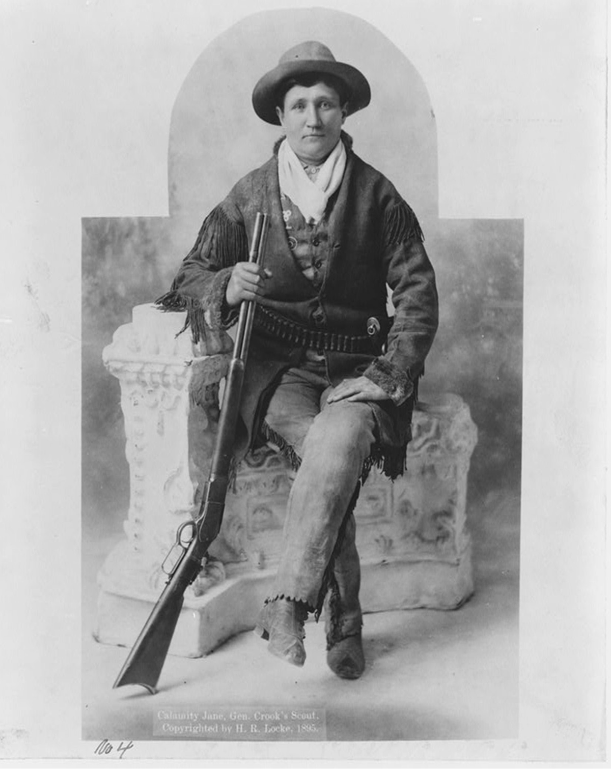A woman in frontier garb poses with a long rifle.