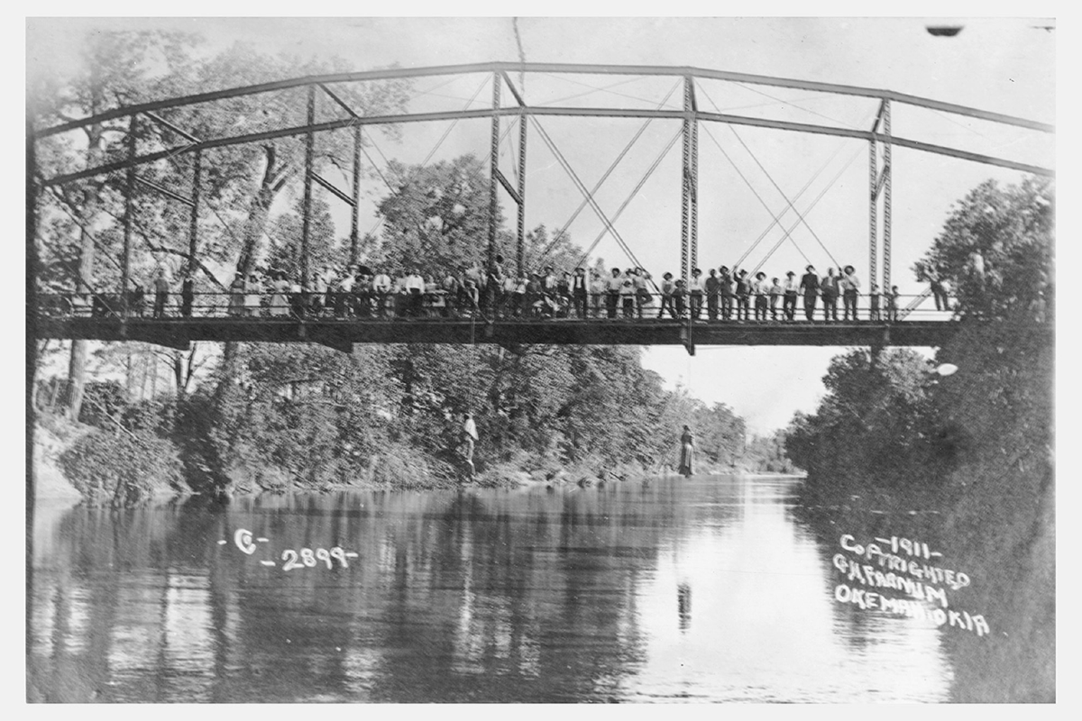 A crowd poses on an iron bridge with two bodies hanging below.