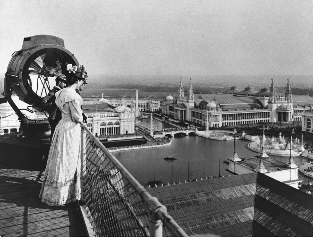 Two men and a woman stand on a rooftop looking down at a fair scene.