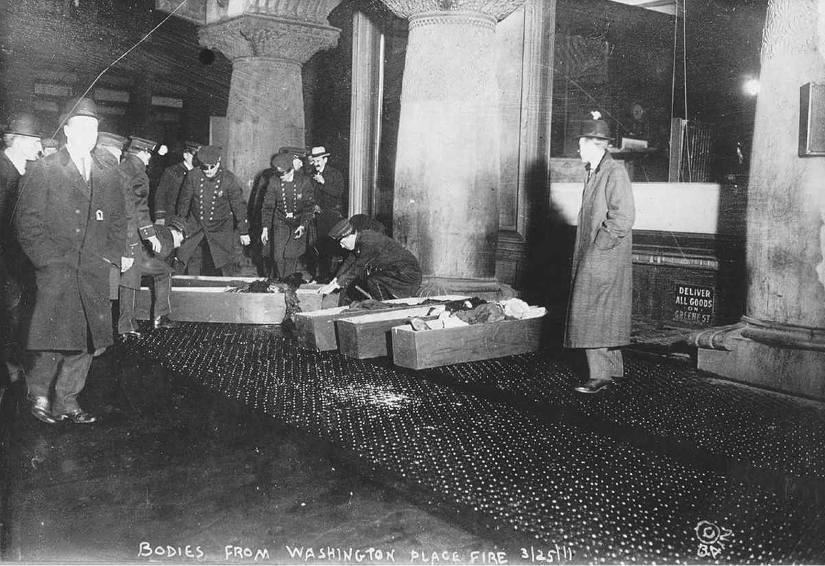 Policemen place bodies into coffins. On the image is written, â€œBodies from Washington Place Fire, 3/25/11.â€