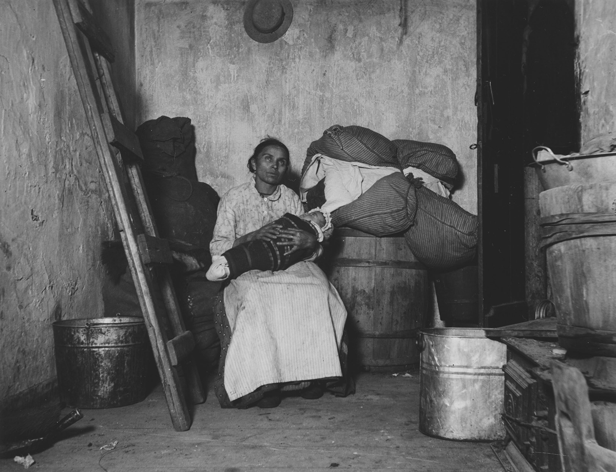 A woman holds an infant in a spare-looking basement room.