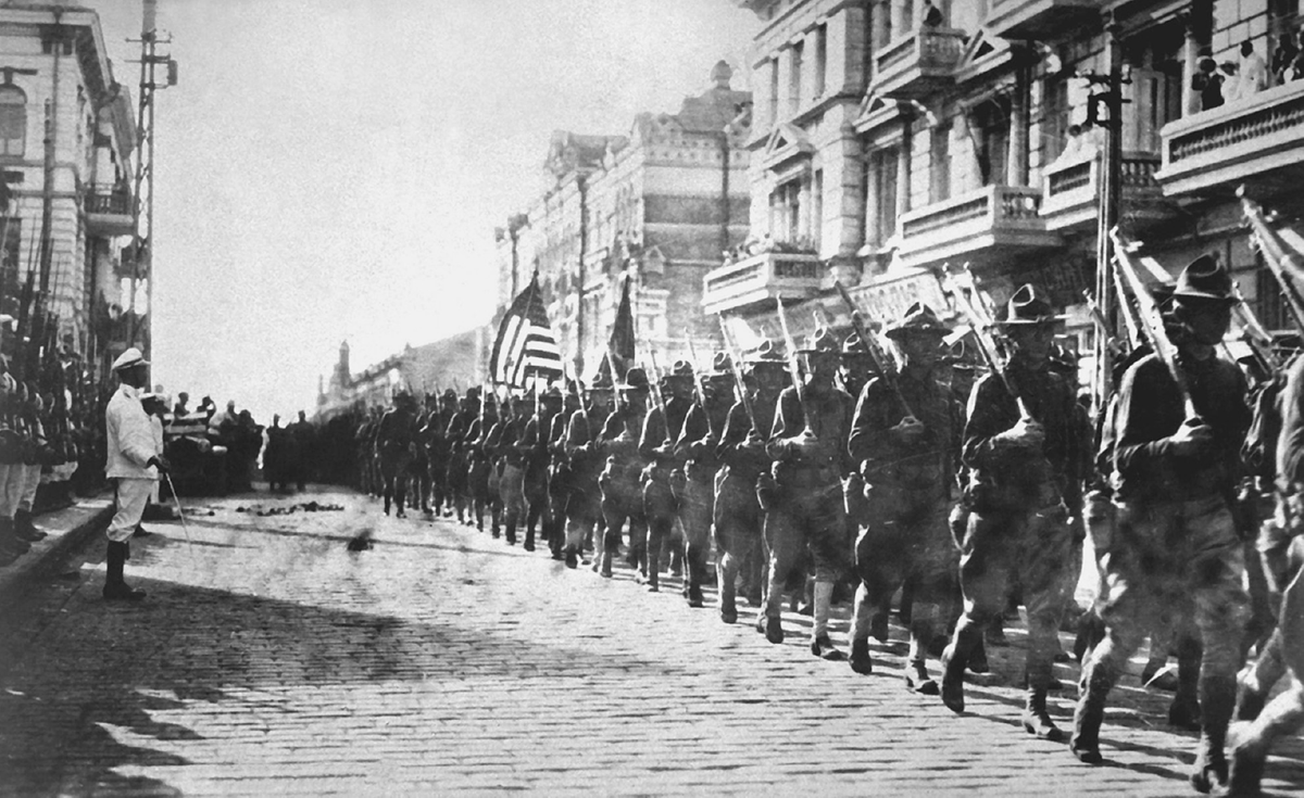 A column of soldiers marches through a city street.