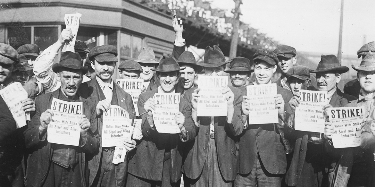 A crowd of men hold up papers headlined “Strike!â€