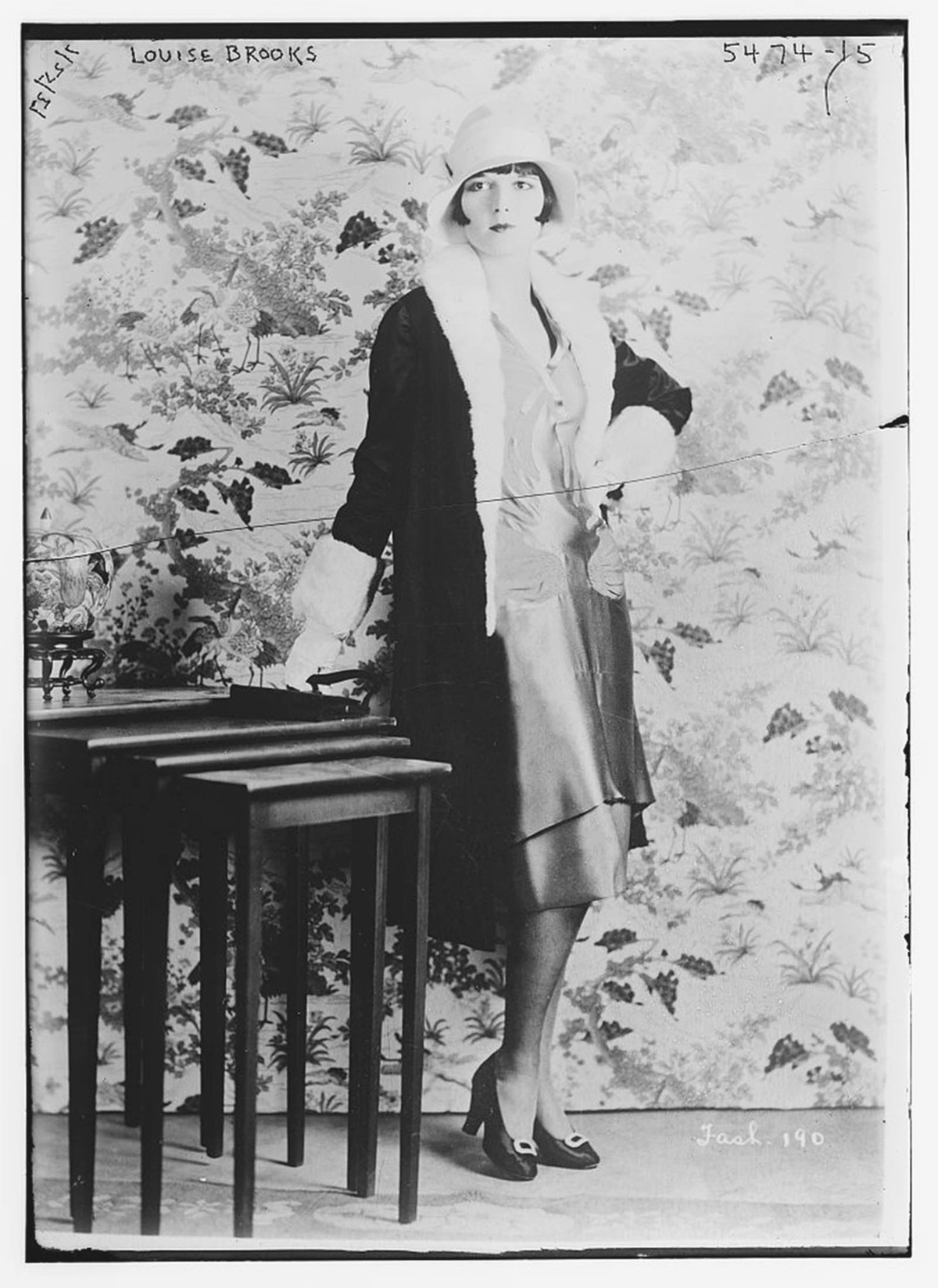 A woman poses next to a side table.