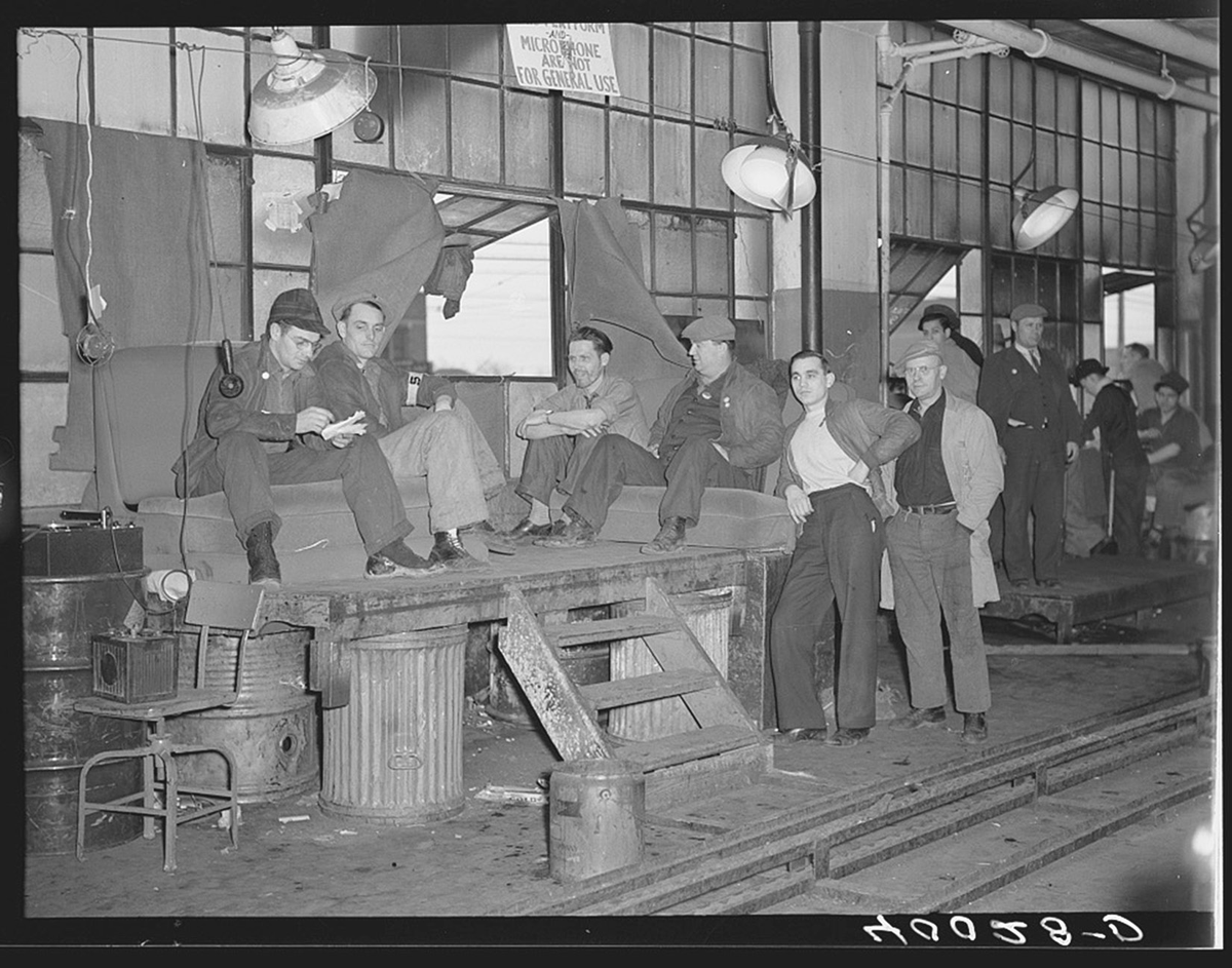 Men lounge outside of a factory building.