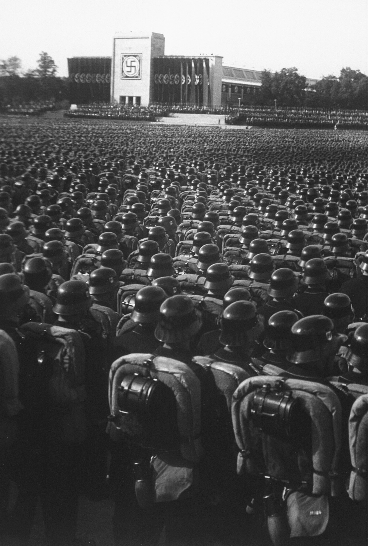 Legions of soldiers stand before a Nazi building.