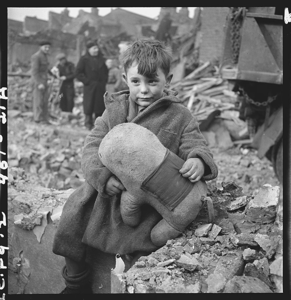 A child, holding a stuffed toy, sits among rubble.