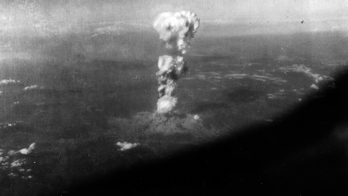 A mushroom cloud rises far in the distance.