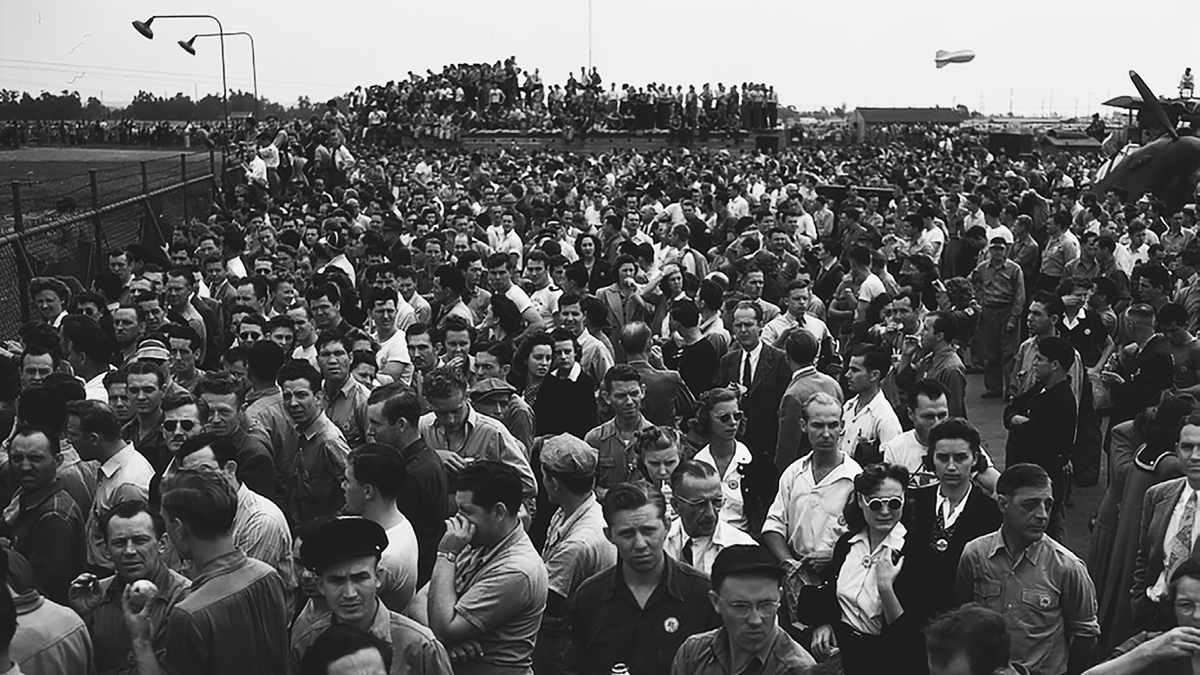 A crowd of workers stands outside of a fence.