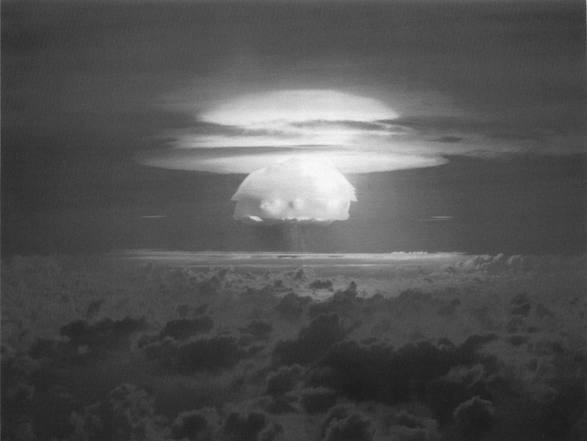 A large mushroom cloud rises in the distance.