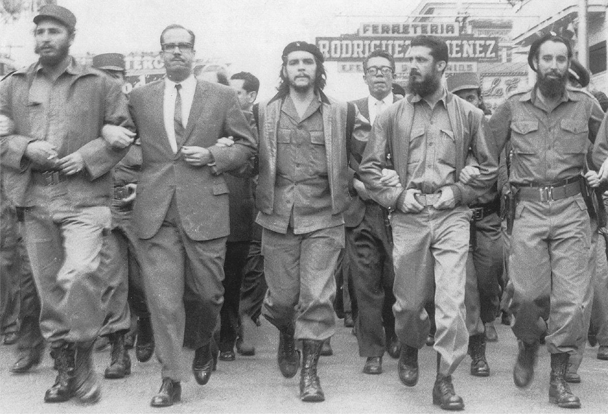 Five men, four in fatigues and one in a suit, march, arm in arm, down a city street.