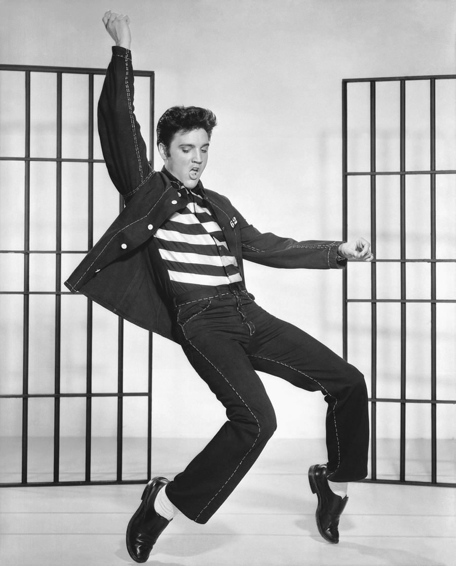 A man in a prison outfit dancing in front of iron jail doors.