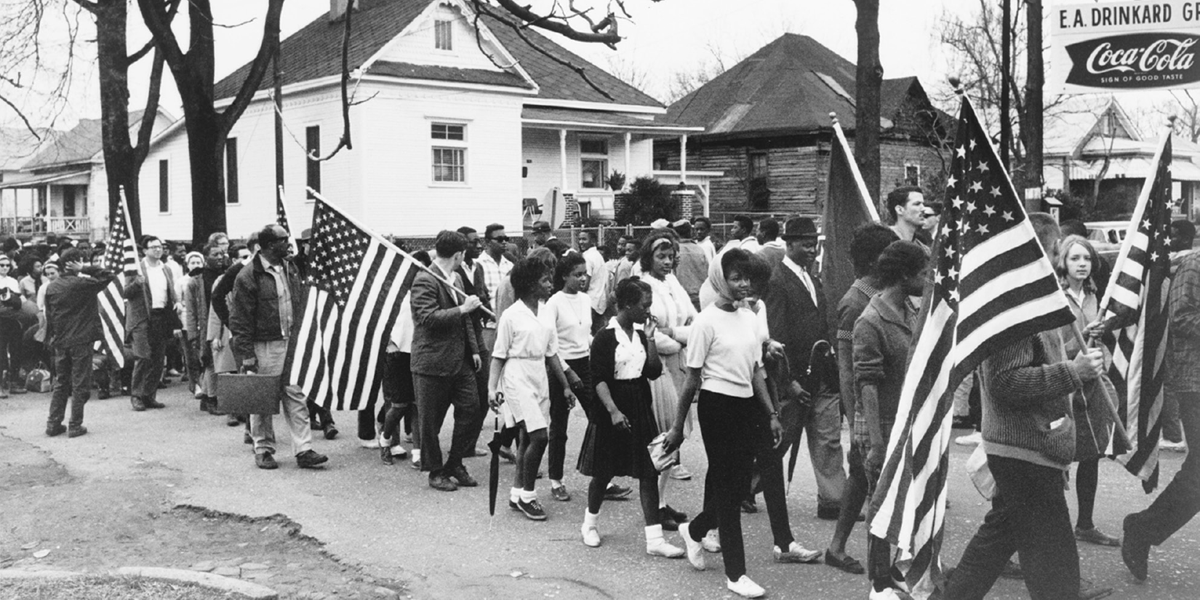 Group of marchers of all ages and races, many carrying American flags.