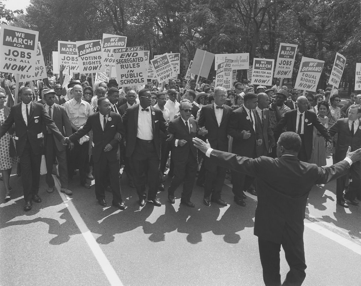 Men and women demonstrate. The placards advocate for jobs, voting rights, and an end to segregation.