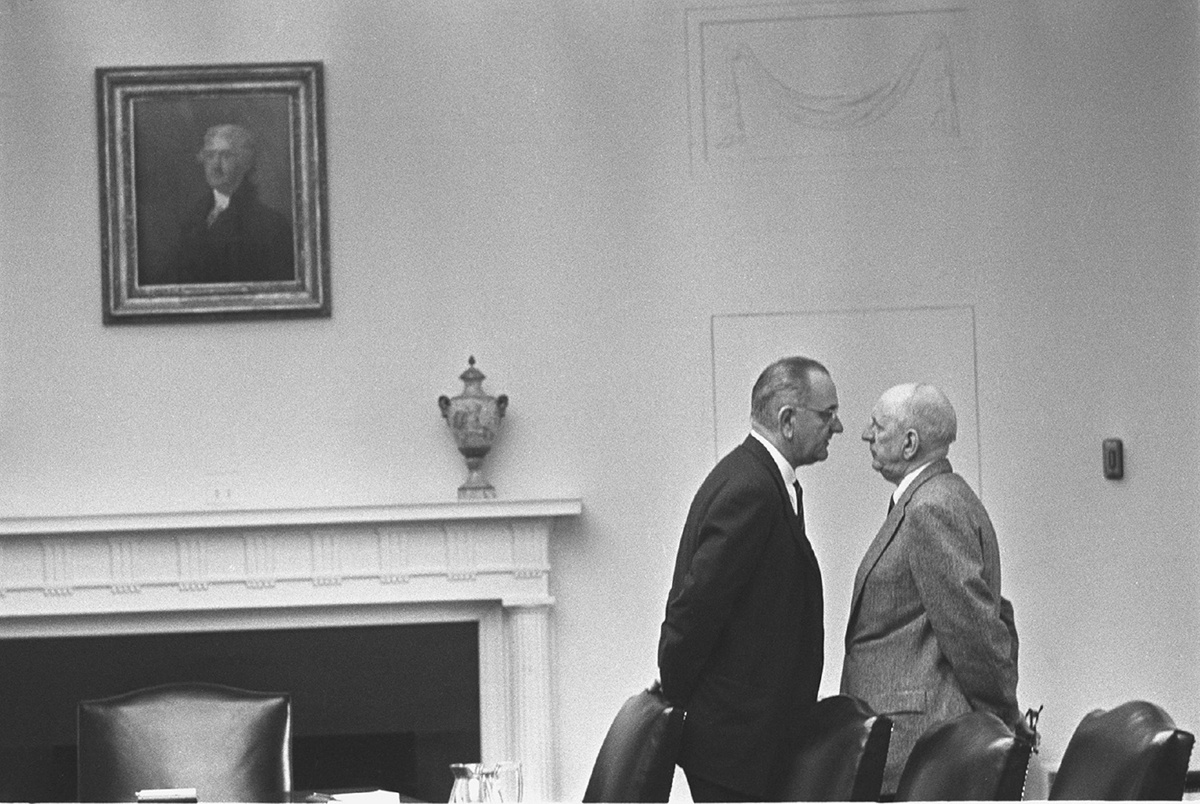 A tall old man in a suit towers over another old man in a suit.