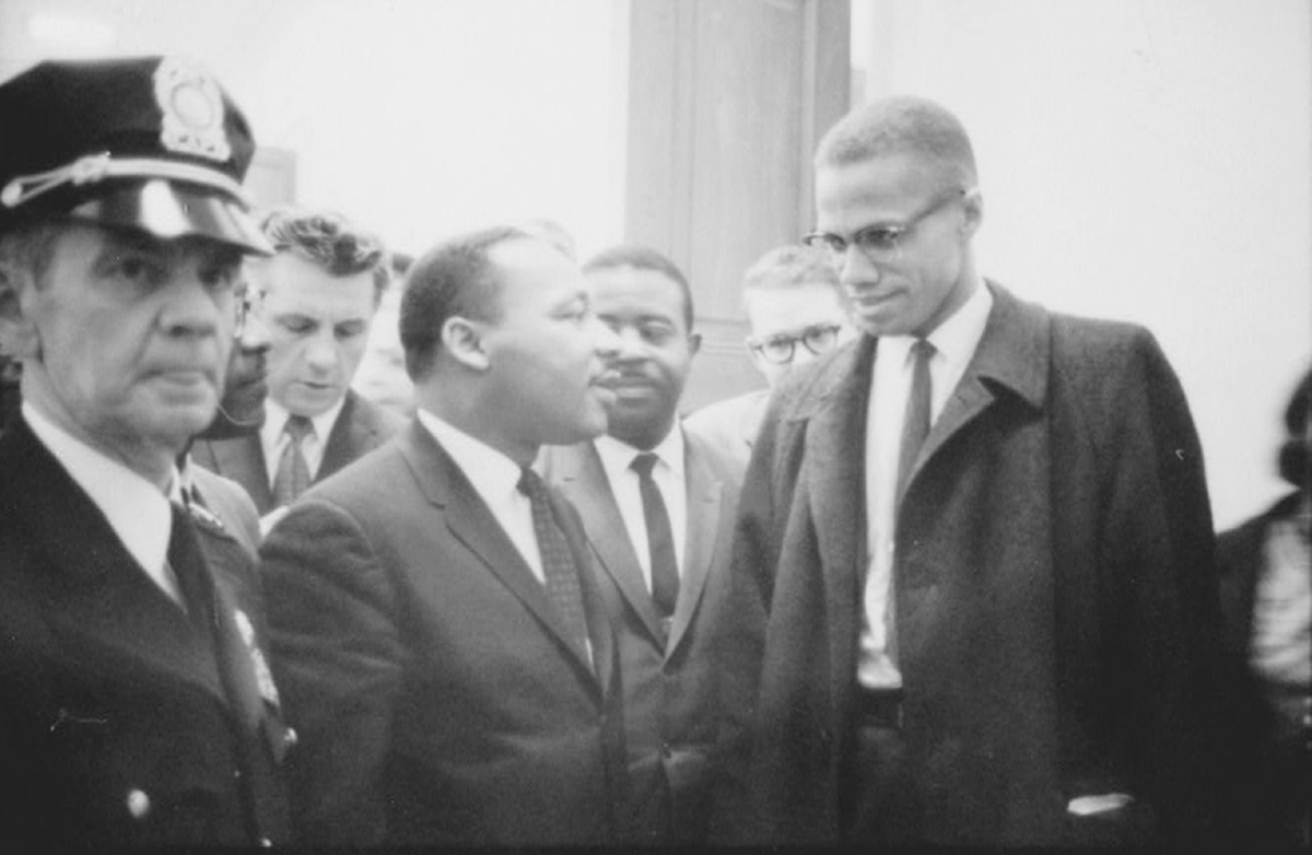 Two men stand next to each other and appear to speak amid a crowd.