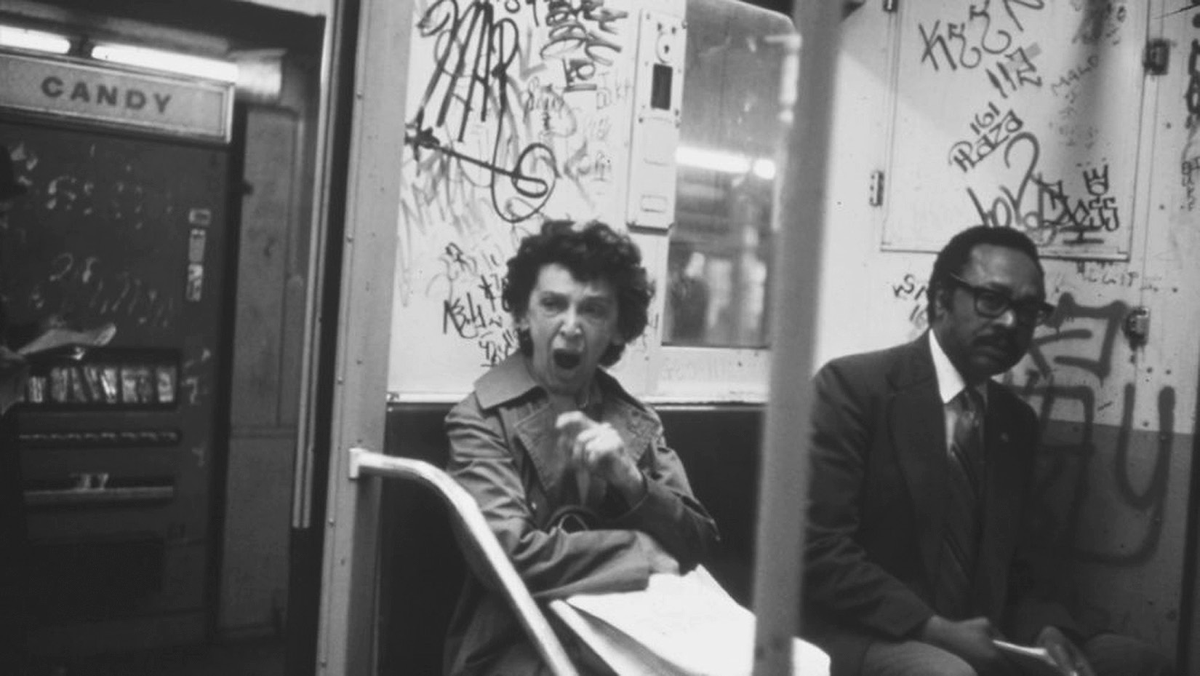 Two riders sit on a graffiti-strewn subway car.