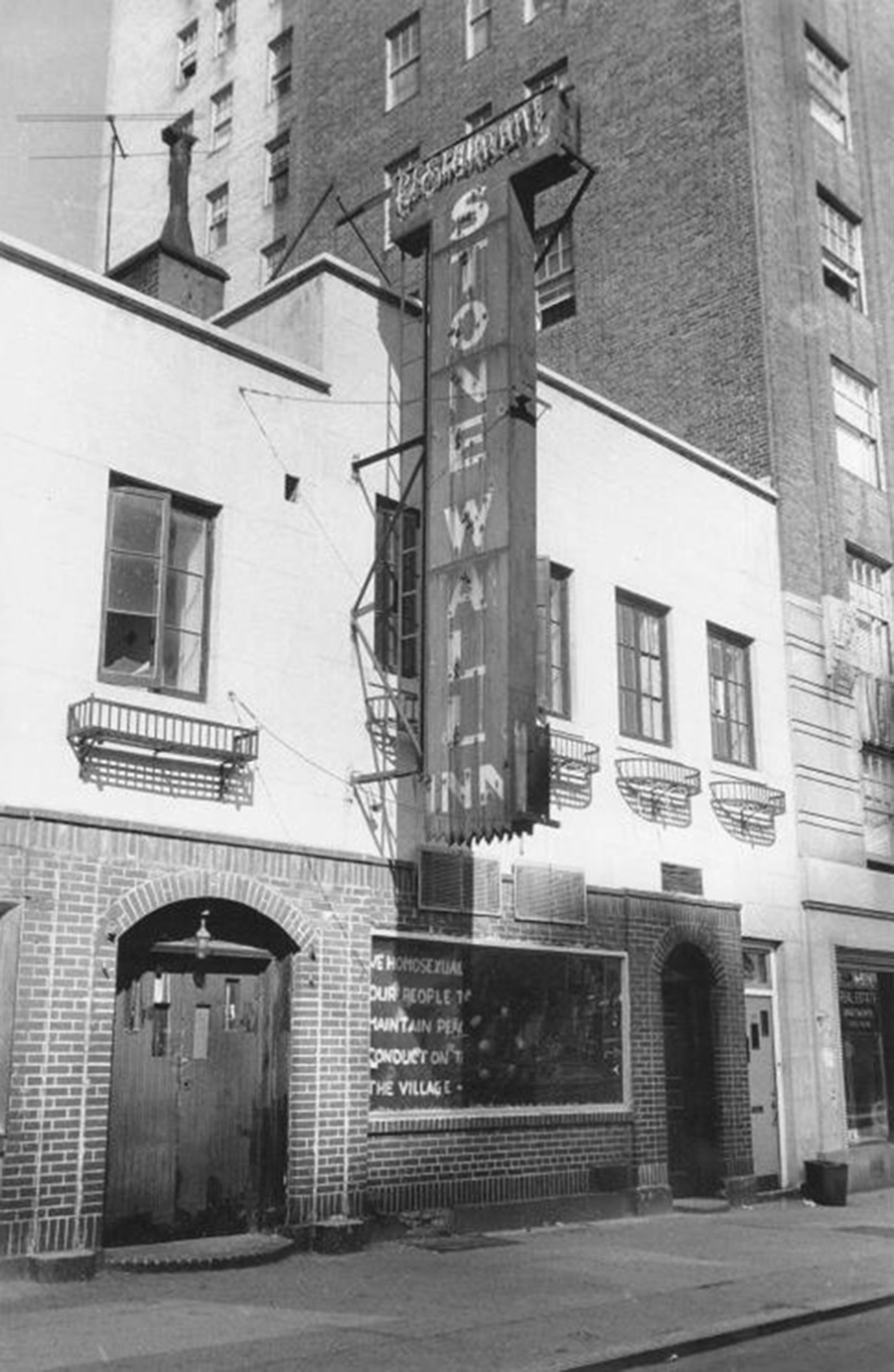 A picture of the Stonewall Inn. A sign in the window reads: â€œWe homosexuals plead with our people to please help maintain peaceful and quiet conduct on the streets of the Villageâ€“Mattachine.â€