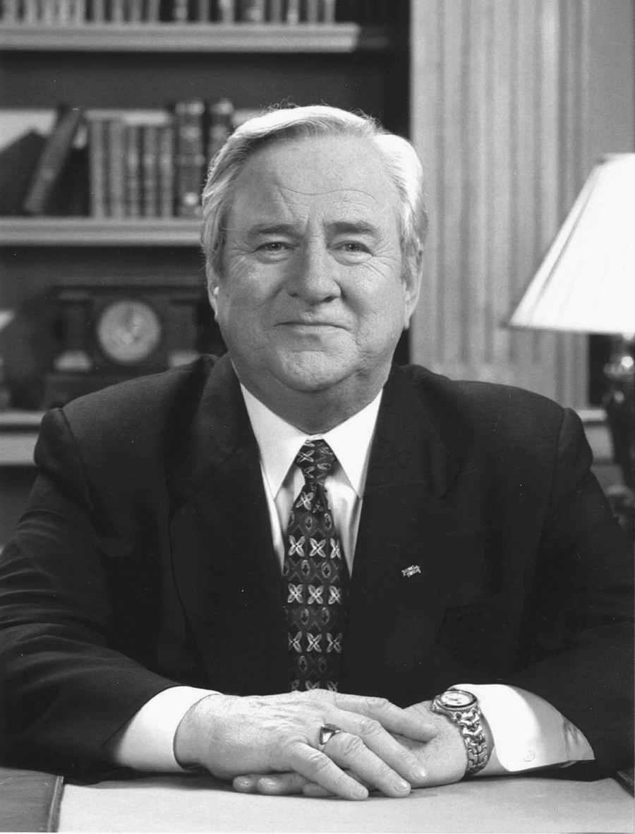 A man in a suit smiles at a desk.