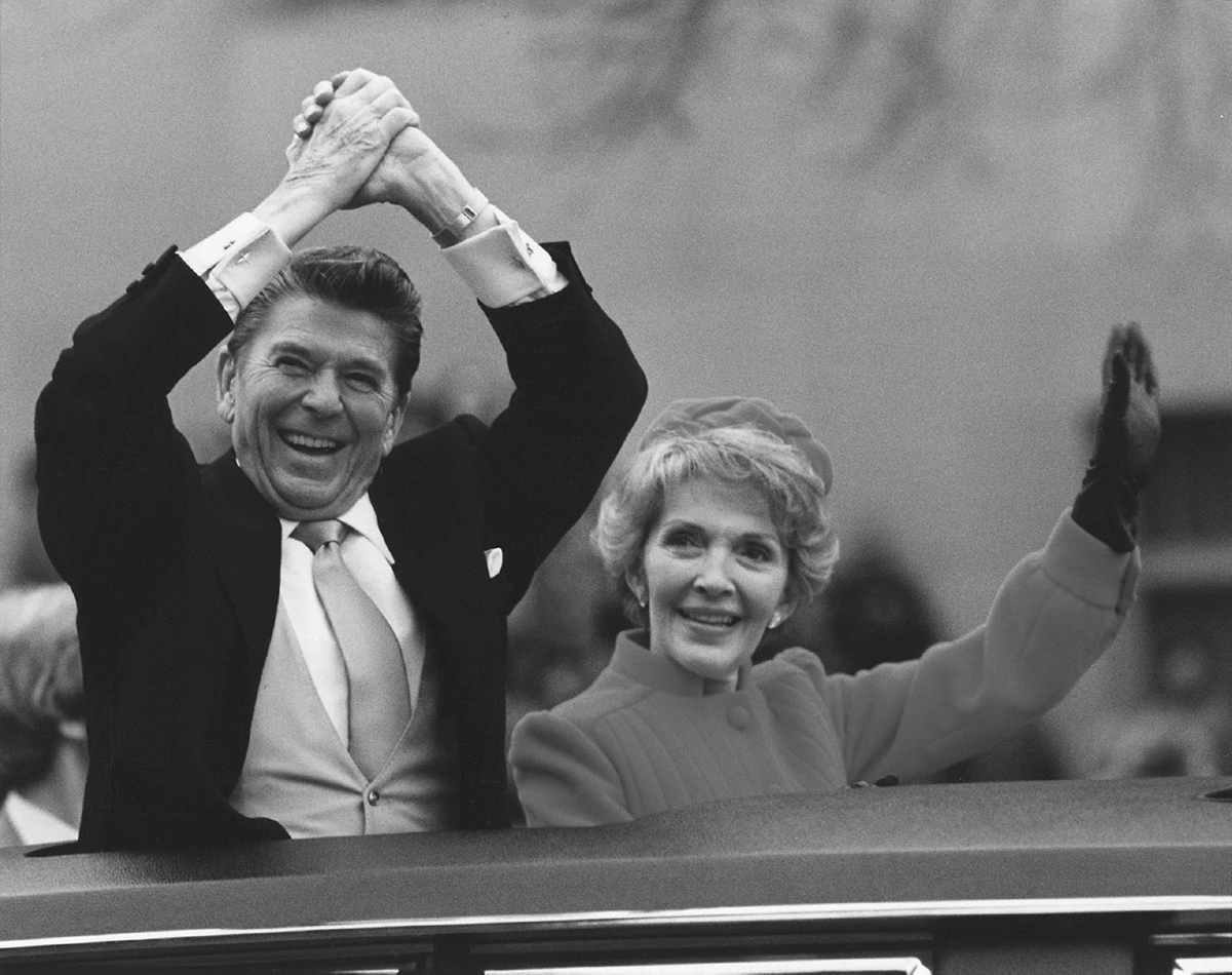An old man cheers and a woman next to him smiles and waves.