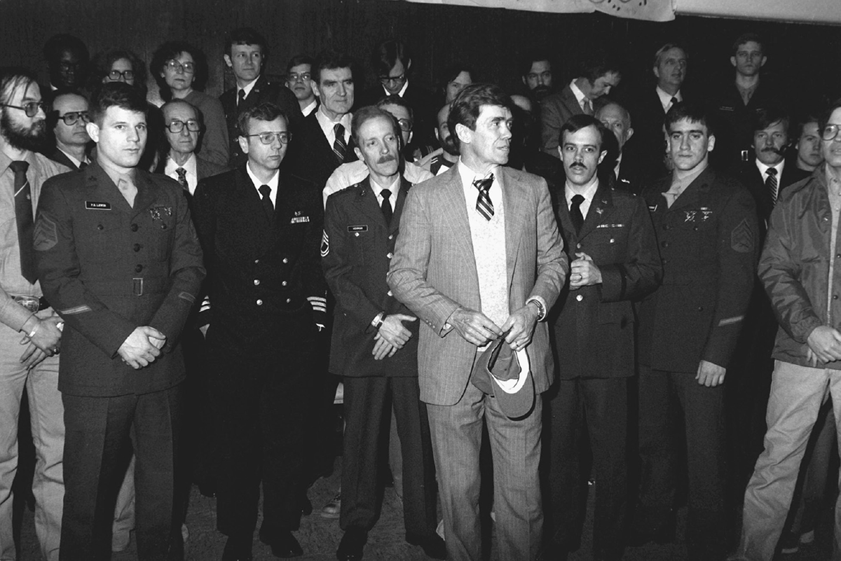 A group of men and women, many in uniform, stand.
