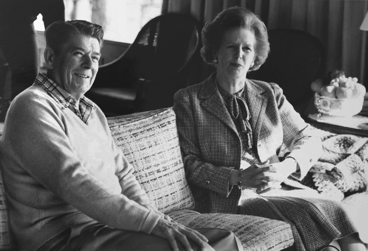An old man and woman pose on a couch.
