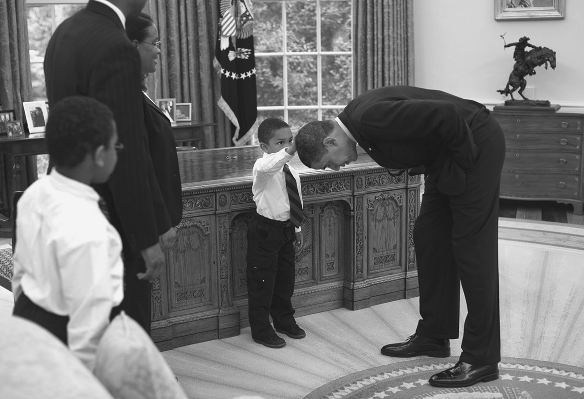 A boy touches the hair of the president in the Oval Office.