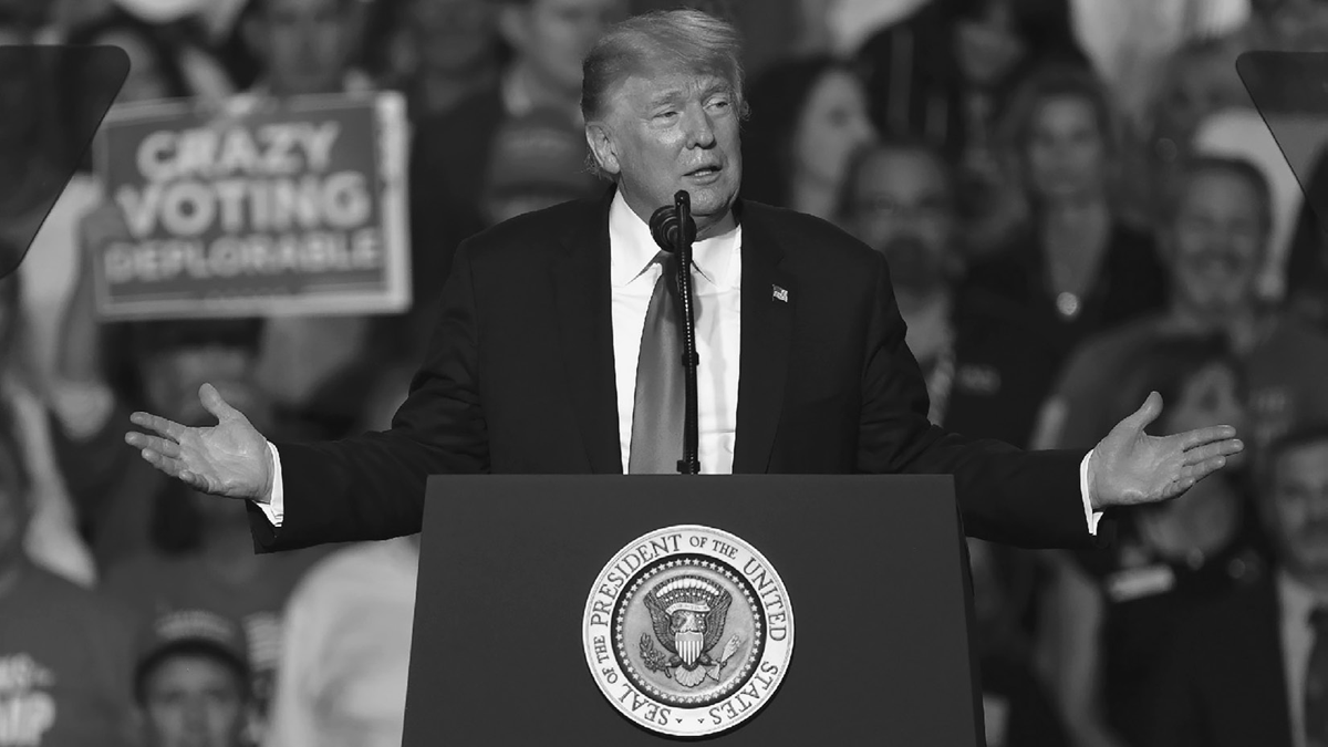 An old man in a suit speaks at a lectern at a political rally.