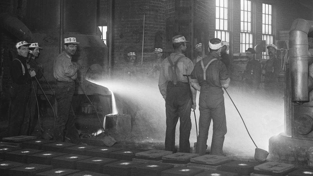 Workers watch as molten glass is poured into molds.