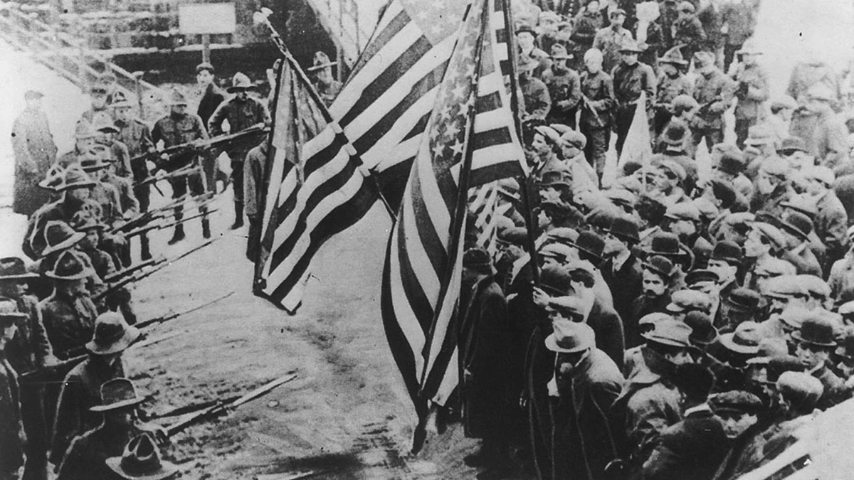Workers bearing American flags face against a line of armed men with rifles and bayonets.