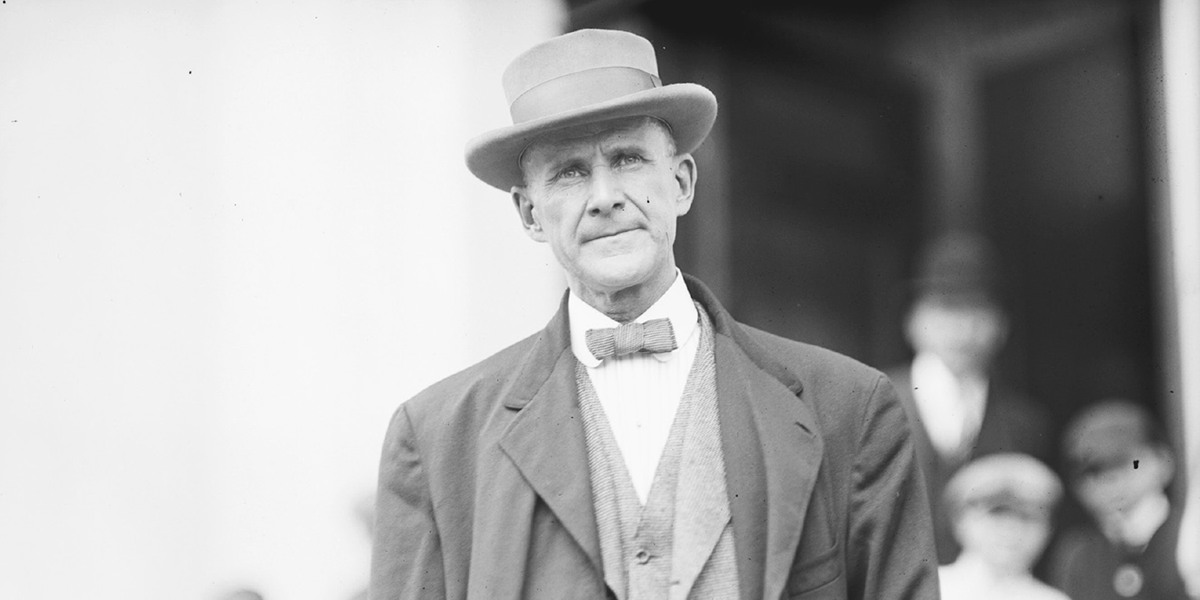 A man in a suit and hat stares into the distance.