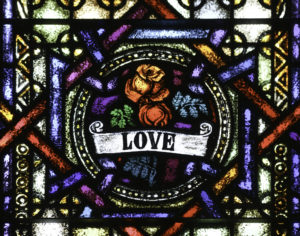 stained glass of an image of flowers with a scroll that reads "love"